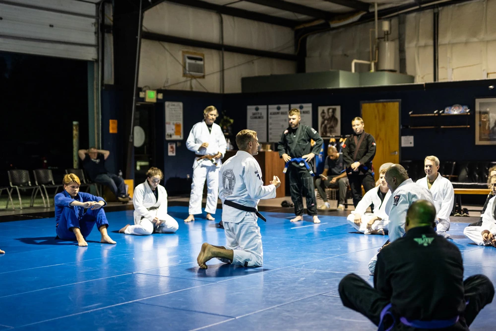 A Method MMA class kneeling on the blue mats while the coach teaches