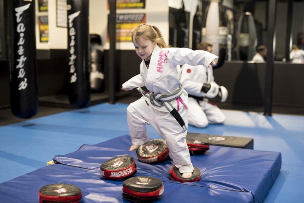 A Little Ninjas student kicking pads held by a coach
